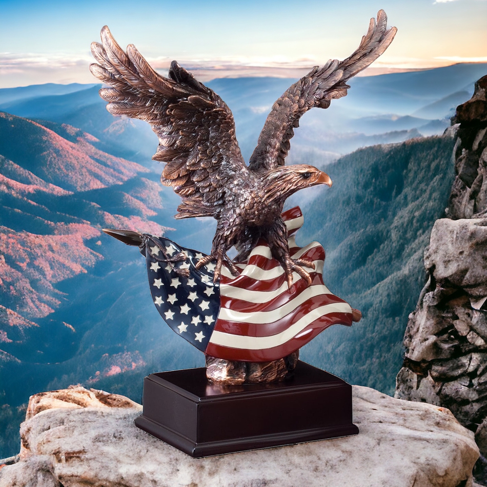 Our Bald Eagle Statue with an American Flag features a bronze eagle statue whose talons are holding an American Flag. It's mounted on a dark wood base that includes an engraving plate for personalization. This specific eagle statue is sitting on a rock high up over looking the valley of a mountain. It comes in 3 sizes to choose from.