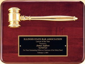 A piano finished rosewood board with a gold metal gavel at the top and a black brass engraving plate at the bottom. The engraving plate has text about the Lawyer of the Year given by the Illinois State Bar Association.