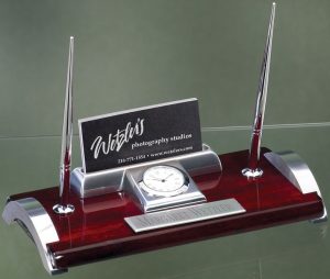 A desk pen set made with piano finished rosewood & chrome silver metal. The set includes a clock, business card holder, 2 silver pens and a silver engraving plate that is personalized with our full color process.