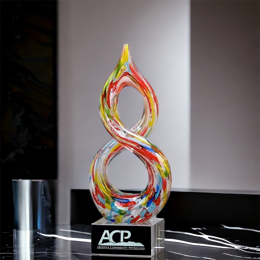 An art glass award in the shape of a helix with numerous colors throughout. It's mounted on a clear glass base with a black & silver engraving plate for personalization. It's sitting on a black marble table top. This glass art award stands 10" tall, weighs 3.4 lbs & comes in a deluxe gift box not shown.