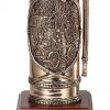 The back of an antique bronze firefighter extinguisher with a very detailed design of an early 1900's firefighter scene. The scene depicts a firefighter steamer and numerous firefighters with ladders fighting the blaze of a large building. The fire extinguisher is mounted on a walnut base.