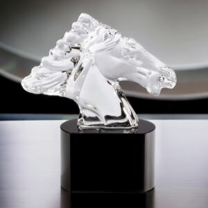 A small crystal horse head trophy. It features a clear crystal horse head on top mounted on a black crystal base. It's sitting on a contemporary desk. It is 5" x 5.5" in size and weighs 3 lbs.