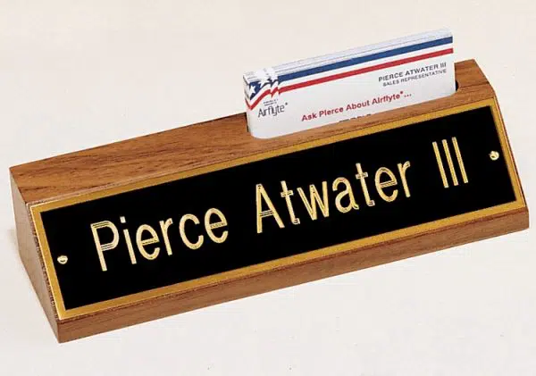 Our Walnut Desk Name Plate With Business Card Holder features an 8" walnut desk wedge made from 100% solid walnut. The top has a place cut out to put display your business card, while the front has a black & gold engraving plate for personalization. This specific one is personalized in gold text for Piece Atwater III. This 535BK is 2.5" x 8" in size and holds 3.5" long business cards.