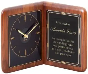 A large walnut clock made in the shape of an open book. The left side features a black faced clock with gold handles, while the right side features a black engraving plate for personalization. This PC850 is 13" x 10" x 5" in size and weighs 3.5 lbs.