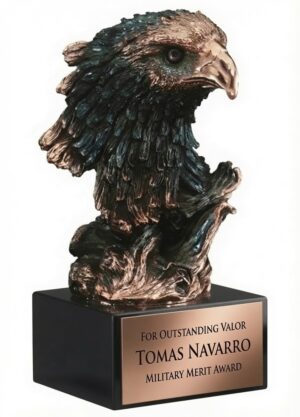 A detailed bronze-finished bald eagle head bust sculpture with intricately textured feathers, sharp beak, and a fierce, piercing gaze. The majestic sculpture is mounted on a sleek black rectangular base featuring a gold engraving plate that reads: 'FOR OUTSTANDING VALOR TOMAS NAVARRO MILITARY MERIT AWARD.' This 10″ tall eagle sculpture includes free engraving or full color personalization.