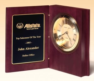 A large book clock with a black & gold engraving plate on the left for personalization and a gold clock with black accents on the right side.
