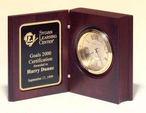 A book clock with a mahogany outside. The left side has a black & gold engraving plate, while the right side has a gold clock. 