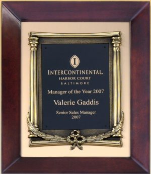 A cherry wood frame with a metal boarder on the inside and an antique bronze finished decorative frame for the black engraving plate. The black engraving plate is laser engraved with gold text & logo.