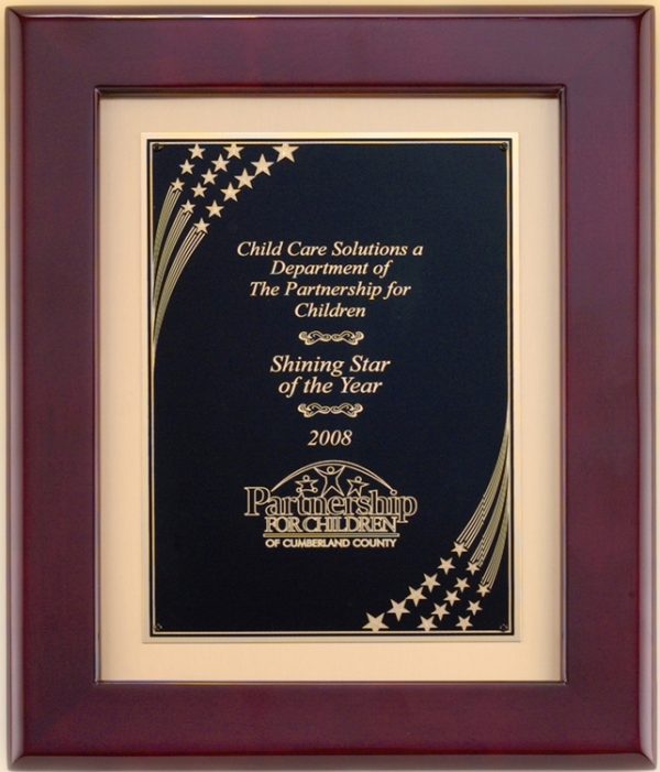 A piano finished frame with a gold inside boarder & a black engraving plate. The engraving plate has a star shower design in the top left and bottom right hand corners of the plate. In the middle is gold engraving of text and a logo.