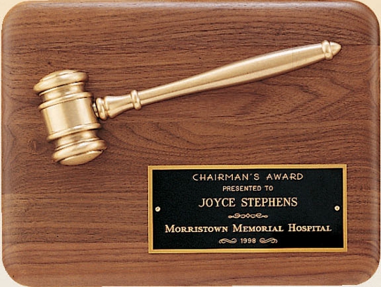 An American walnut board with rounded corners. Towards the top of the walnut plaque is a gavel with an antique gold cast color. In the bottom right hand corner is a black brass engraving plate. On the plate are words of appreciation for the Chairman's Award given by Morristown Memorial Hospital.