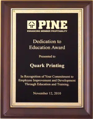 An award plaque with a cherry board and a black & gold engraving plate with a Florentine border. The gold engraving on the plate features a company logo and words of appreciation for an employee.
