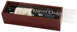A rosewood finished wine box with an acrylic lid for personalization. It easily slides in and out with the use of a finger hole at one end. The inside of the box is lined with black satin & it holds a bottle of Robert Mondavai wine.