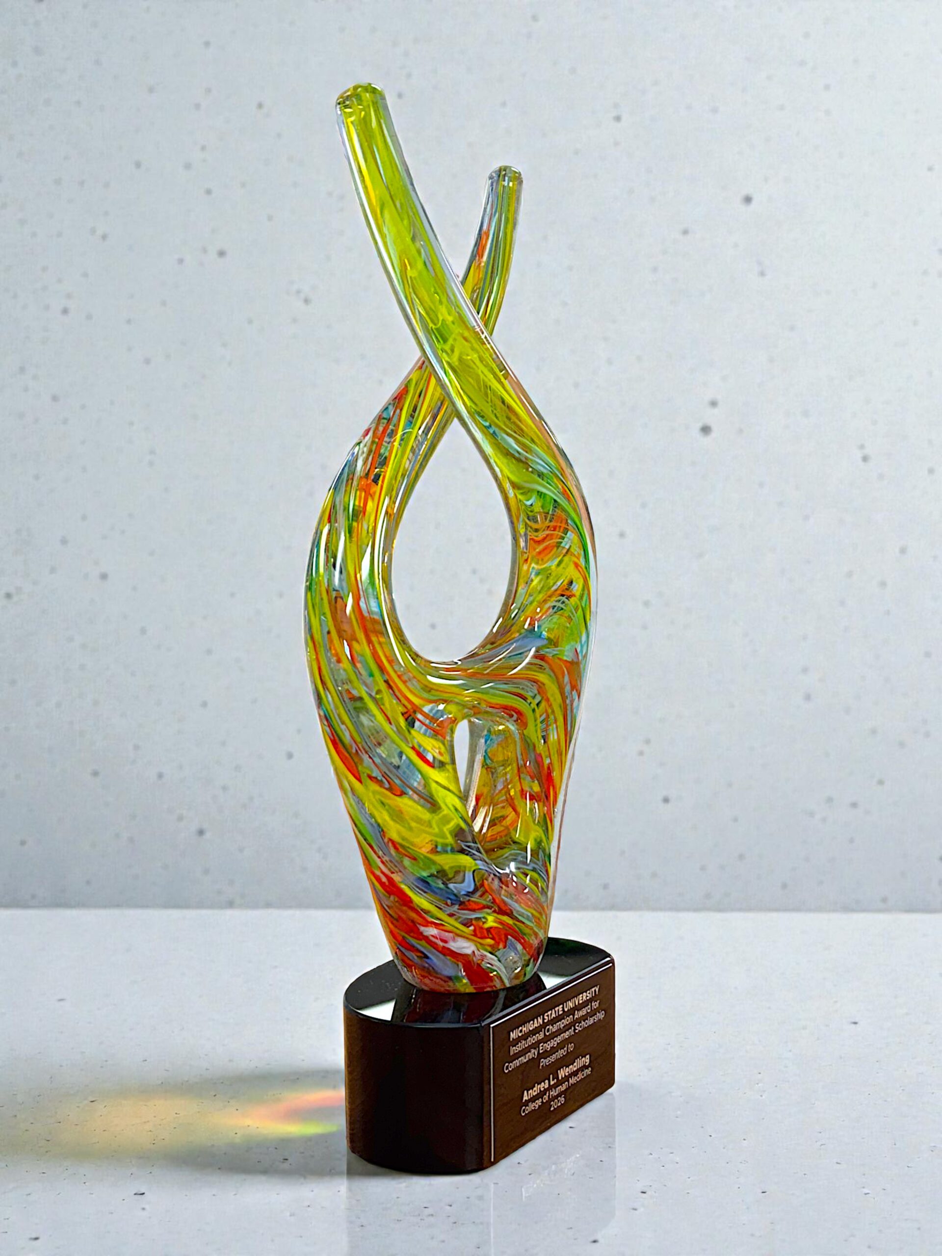 Our Color Twist Glass Art Award is mounted on a black glass base with a black & gold engraving plate for personalization. This photo shows the item at an angle showing the items left side.This item comes packaged in a satin lined, deluxe gift box.
