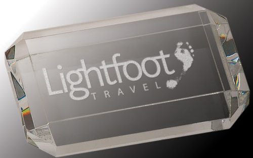 A rectangle crystal paperweight with beveled edges on the sides. In the middle is a laser engraved version of the Lightfoot Travel logo.