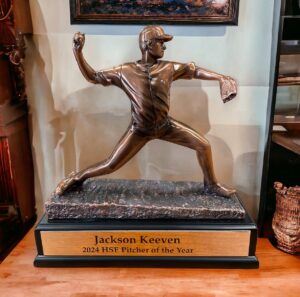 Our Baseball Pitcher Trophy features a resin statue coated in a glossy resin bronze metal. The statue is a baseball pitcher in the middle of his pitch as he throws to home plate. It's mounted on a black base that includes an engraving plate for personalization. This one is personalized for Jackson Keeven, the 2024 HSE Pitcher of the Year. This RFB041 baseball trophy is 9" x 8.5" in size and weighs 2.5 lbs.