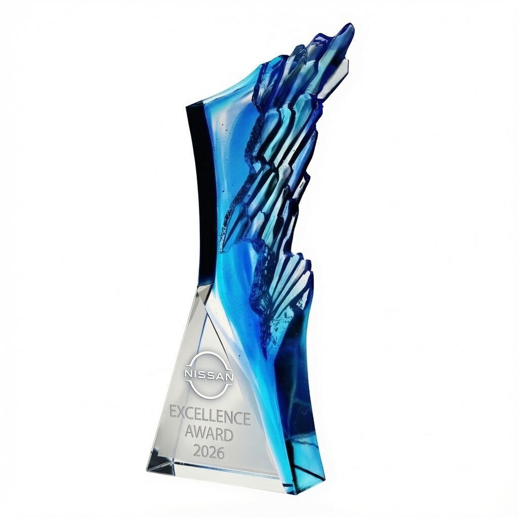 Blue Crest Crystal Award (C2463) featuring a striking handcrafted optic crystal design with vibrant blue pâte de verre accents resembling a dynamic coastal wave or arctic crest. The clear crystal base is laser engraved with the official Nissan logo above the text 'EXCELLENCE AWARD 2026' in elegant frosted lettering. This modern 10-1/8 inch tall premium recognition trophy stands on a solid base and is perfect for corporate achievement awards.