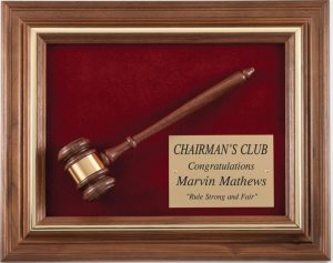 A genuine walnut frame with a gold inlay. Inside the frame is a maroon velour background with a walnut gavel & gold engraving plate on top. The gold engraving plate is recognition for a Chairman's Club Award.