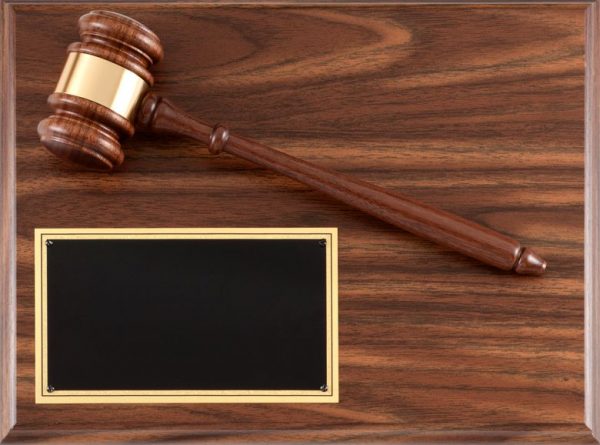 A walnut finish board with a walnut gavel & gold gavel band. It's slanted downward from the top left to the middle right. In the bottom right hand corner is a black engraving plate for personalization.