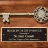 A 9x12 walnut board with a cast a cast metal, large decorative key at the top. Below is a black brass engraving plate for personalization. The engraving is for The Key to the City of Branson and it's presented to Samuel Carola.