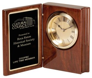 A walnut book clock that features a piano finish outside, a black & gold engraving plate on the left side and a gold clock with black accents on the right side.