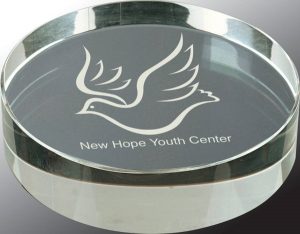 A round crystal paperweight that is 3/4" thick. A logo for New Hope Youth Center is laser engraved on the bottom. 