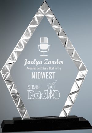 A diamond shaped glass award with a diamond stainless steel look around the edges. The inside has laser engraving of an old radio microphone. It's an award for Best Radio Host in the Midwest. The clear glass piece is mounted on a black glass base.