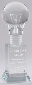 A crystal award featuring a solid crystal light bulb mounted on a crystal pillar. The pillar has laser engraving about a "Bright Idea Award."