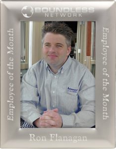 A silver metal picture frame that features a photo of an employee. The frame features laser engraving. The top of the frame features a company logo, the bottom has the employee's name & the sides read "Employee of the Month."