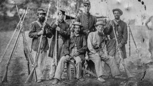 Soldiers from the Civil War wearing hats and holding their musket rifles.