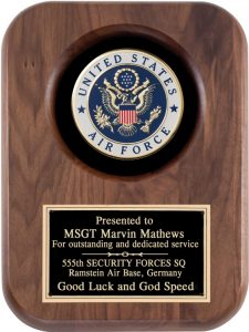 A solid walnut plaque with rounded corners. The middle top features a full color Air Force Seal, while the bottom features a black & gold engraving plate with words of recognition for dedicated service.