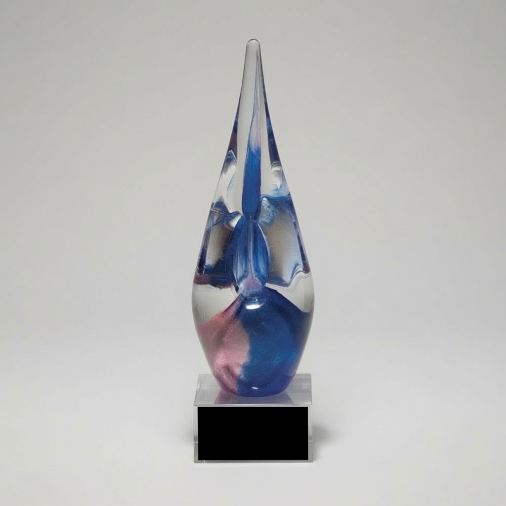 Modern abstract blue and violet art glass trophy featuring a tall, elegant teardrop-shaped hand-blown glass sculpture with swirling patterns of deep blue, vibrant violet, pink, and clear crystal. The glass award sits on a thick clear rectangular acrylic base with a blank black plaque area. Professional studio photograph on a light gray background.