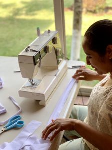 A woman from El Refugio learns to sew. She has a white blouse on and she's working with a white sewing machine and white material.