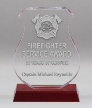 Elegant clear crystal trophy with a graceful curved shield shape and vibrant pink/magenta accents. Mounted on a rich red crystal base, this modern award is perfect for achievement recognition, corporate milestones, and special presentations."