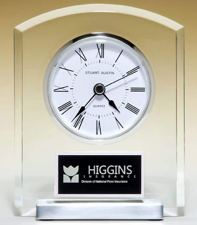 An acrylic desk clock with a dome shaped top. It has a white clock face, silver bezel, a silver metal base and a black & silver engraving plate.