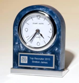 An acrylic clock with a polished blue marble look that has a white clock face & silver bezel. Below the clock face is a blue & silver engraving plate that's personalized with a logo & name. The base of the clock is made with silver aluminum.