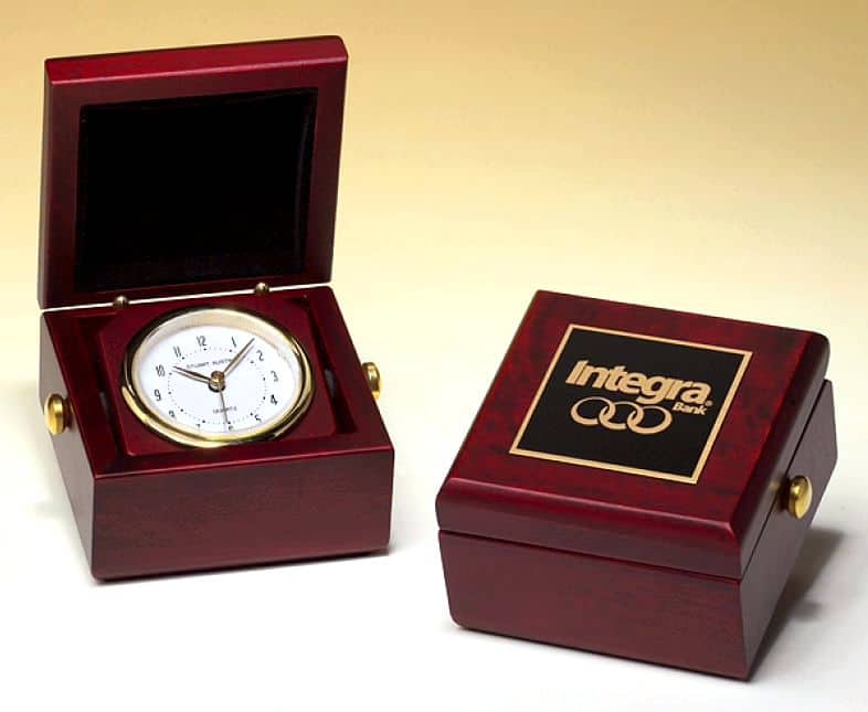 On the left is our Small Captain's Desk Clock open. It shows a white clock face with gold accents. There's also gold metal knobs on each side and the top of the inside of the box is lined with black velour. On the right is the same clock, but it is closed. It's showing off the black & gold brass engraving plate with a logo of a company laser engraved into it.