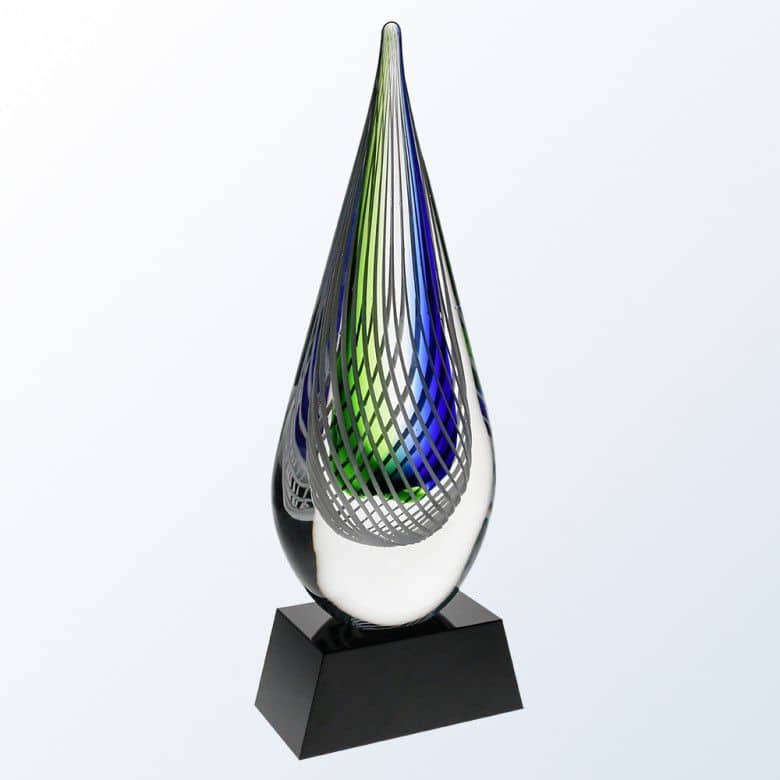 A raindrop shaped piece of clear glass with blue & green colors in the middle. There's a frosted white netting design closer to the front of the surface for added decoration. The glass raindrop is mounted on a black glass base.