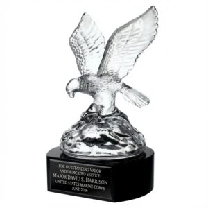Soaring Eagle Crystal Award (SKU: G1250B) featuring a detailed, fully spread-wing crystal eagle sculpture mounted on a solid black crystal base. The award measures 9.75″ tall x 6.125″ wide x 5.5″ deep and weighs 7.8 lbs. The black base includes a silver-engraved plate with the text: 'FOR OUTSTANDING VALOR AND DEDICATED SERVICE / MAJOR DAVID S. HARRISON / UNITED STATES MARINE CORPS / JUNE 2026'. This premium patriotic military recognition trophy symbolizes strength, leadership, and achievement.