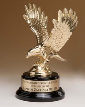 A shiny gold finished eagle made from metal with it's wings spread. It's mounted on a black piano finished base that also has a gold engraving plate for personalization. this 1298/XL eagle statue stands a total of 9" tall.