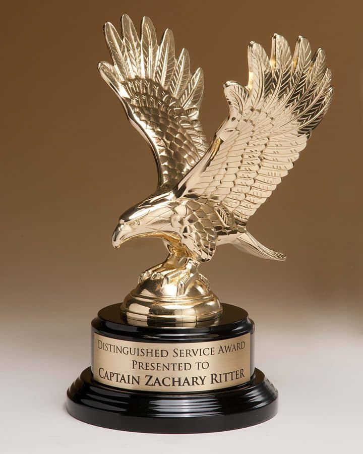 A shiny gold finished eagle made from metal with it's wings spread. It's mounted on a black piano finished base that also has a gold engraving plate for personalization. this 1298/XL eagle statue stands a total of 9" tall.