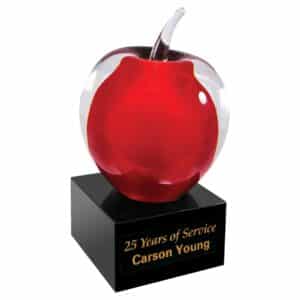A glass apple that has red color on the inside. The glass apple is mounted on a black glass base with an engraving plate for personalization.