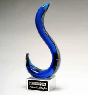 An art glass award in the shape of a hook. The majority of it's color is blue, but there are other accent colors such as red, yellow & green. It's mounted on a clear glass base with a black & silver engraving plate for personalization.