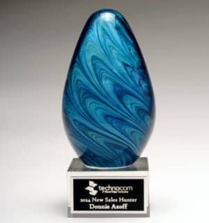 An art glass award featuring a blue marble glass egg mounted on a clear glass base. The base has a black & silver engraving plate for personalization. This 2313 glass award stands 6.25" tall, comes in a deluxe gift box & includes free engraving.