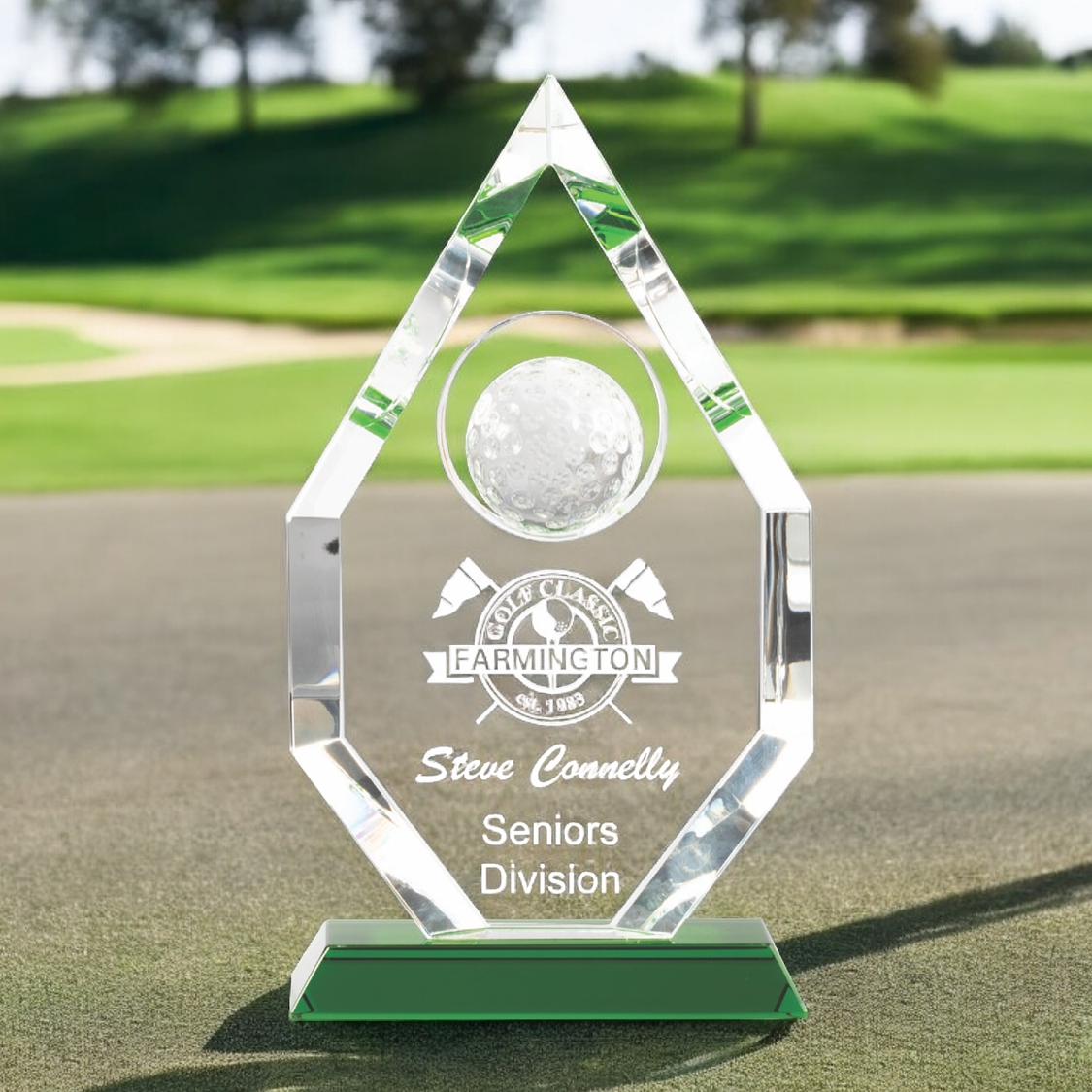 Our Crystal Peak Award features beveled piece of crystal with a solid crystal golf ball at the top & a blank area for engraving below. It's mounted on a green crystal base. This CRY954 stands 10.25" tall & weighs 4 lbs. This award is show on a golf green with a bunker, sand trap & trees in the background.