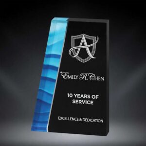 Blue Wave Acrylic Award featuring a sleek black trapezium-shaped acrylic with a vibrant blue wave design on the left side. Engraved in white with a stylized 'A' shield logo, 'Emily R. Chen', '10 Years of Service', and 'Excellence & Dedication'. Modern custom recognition trophy.